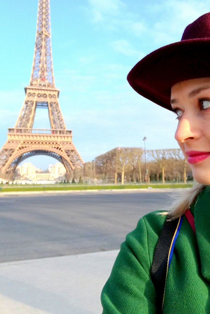blond_girl_in_a_hat_standing_next_to_the_eiffel_tower